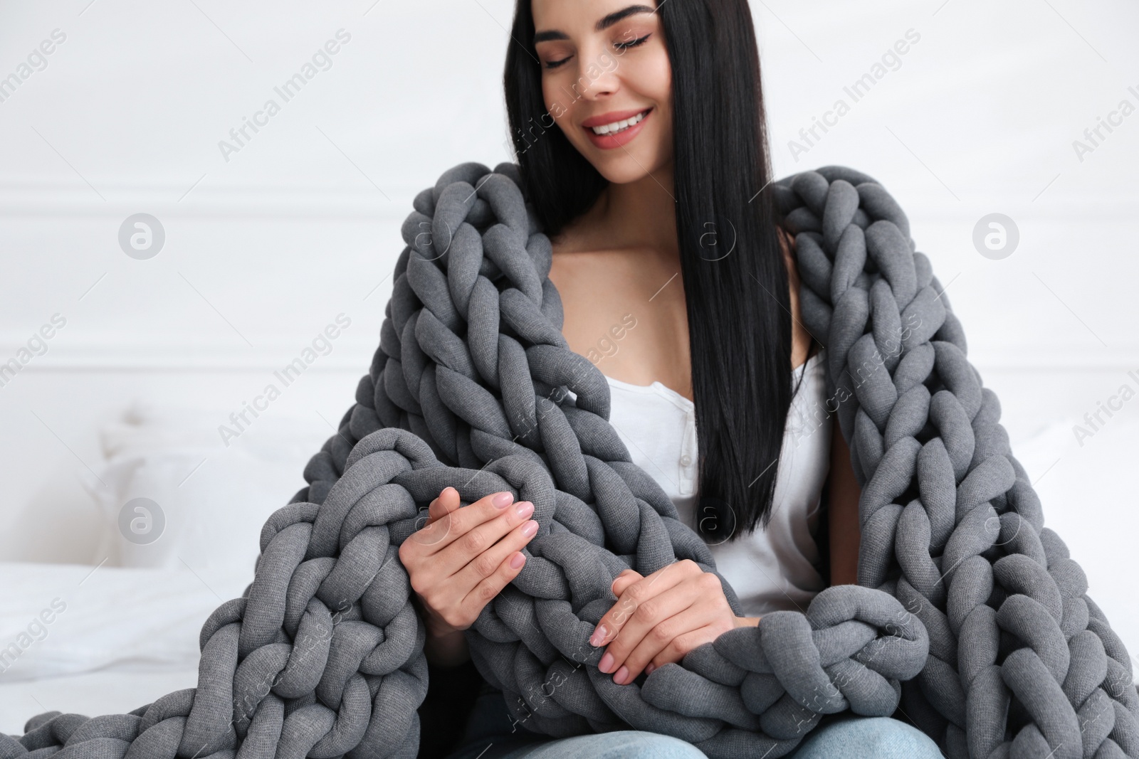 Photo of Young woman with chunky knit blanket on bed at home