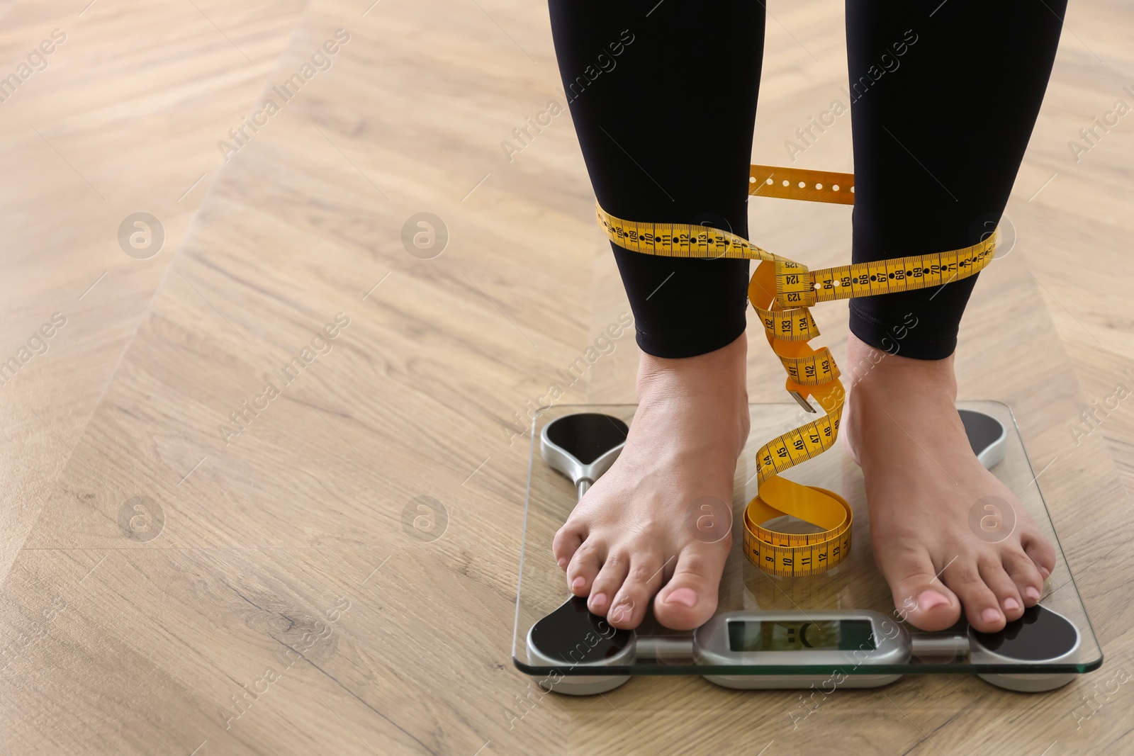 Photo of Closeup view of woman tied with measuring tape using scale on floor, space for text. Overweight problem after New Year party