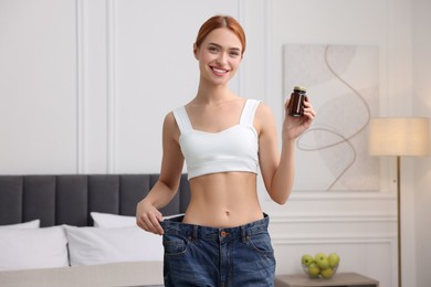 Photo of Slim woman in big jeans with bottle of pills at home. Weight loss