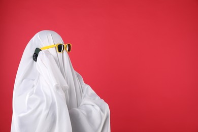 Person in ghost costume and sunglasses talking on smartphone against red background, space for text