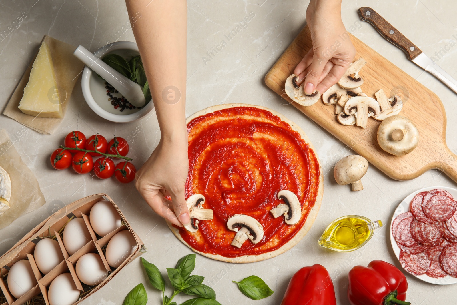 Photo of Woman putting mushrooms onto pizza crust with sauce on light table, top view
