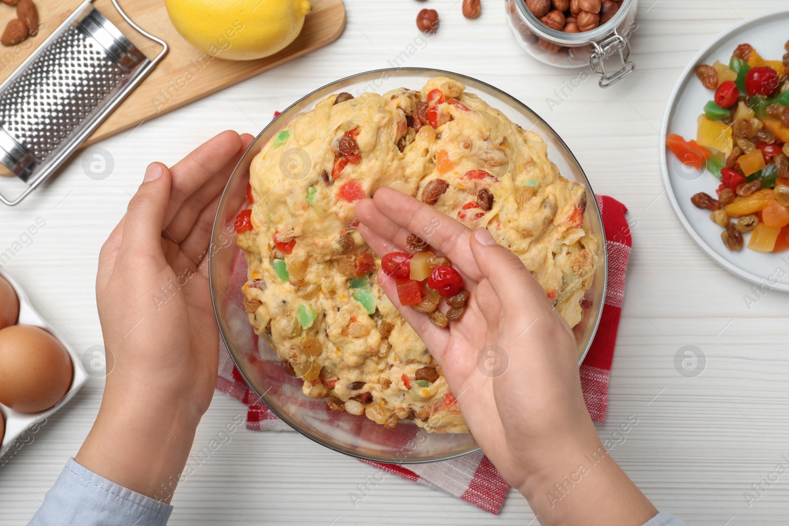 Photo of Woman adding candied fruits to dough for Stollen at white wooden table, top view. Baking traditional German Christmas bread