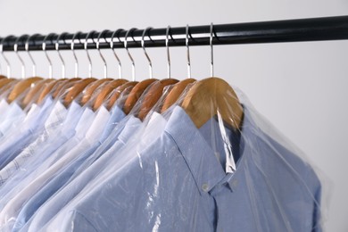 Photo of Hangers with shirts in dry cleaning plastic bags on rack against light background