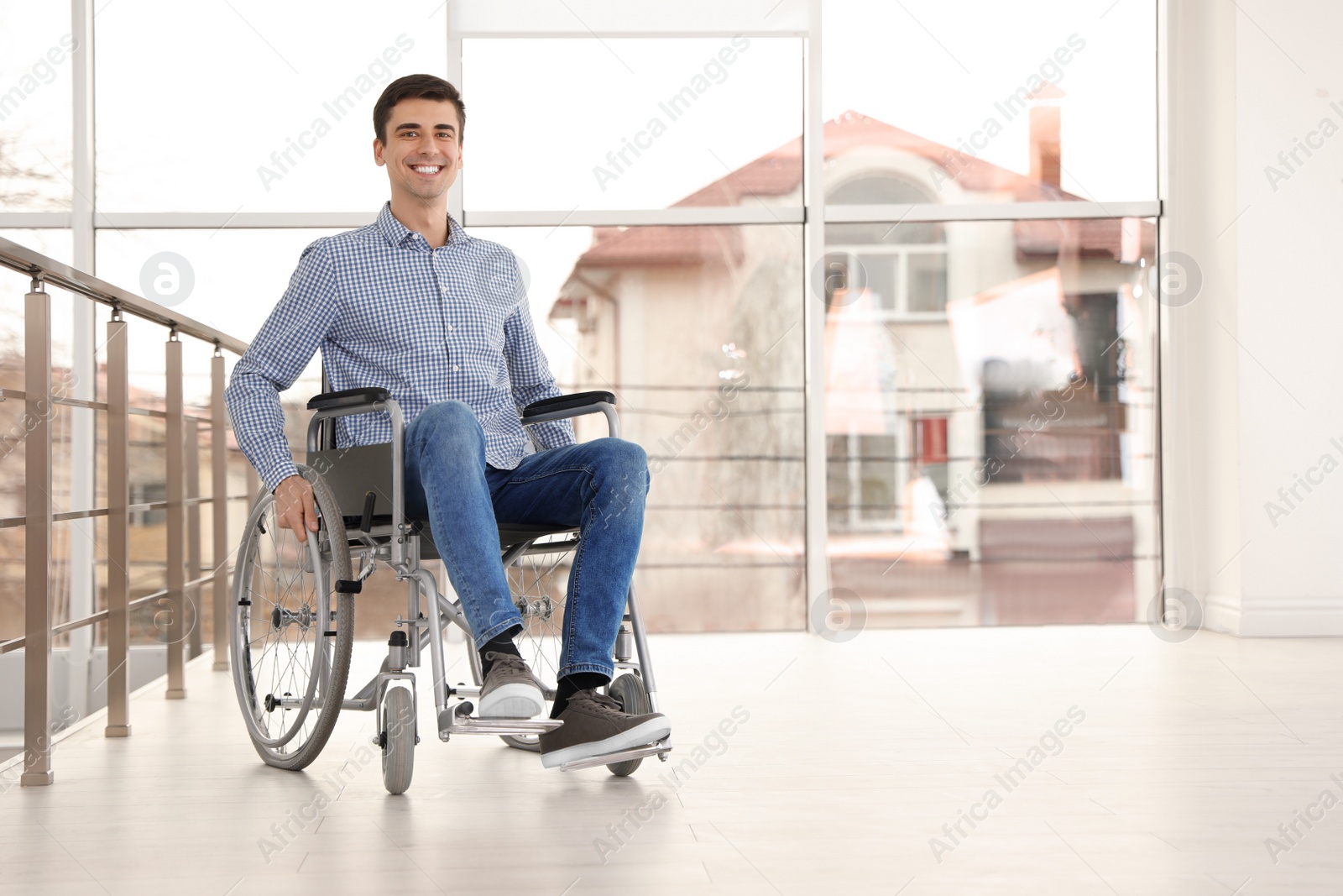 Photo of Young man in wheelchair near window indoors. Space for text