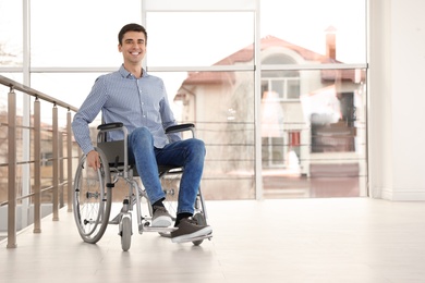 Young man in wheelchair near window indoors. Space for text