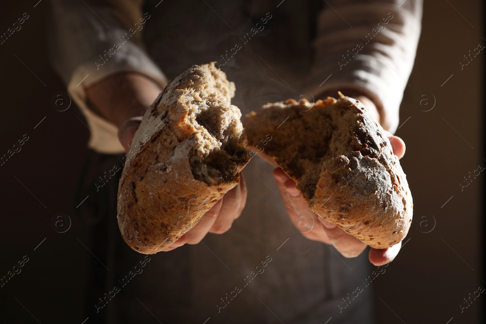 Photo of Man breaking loaf of fresh bread on dark background, closeup