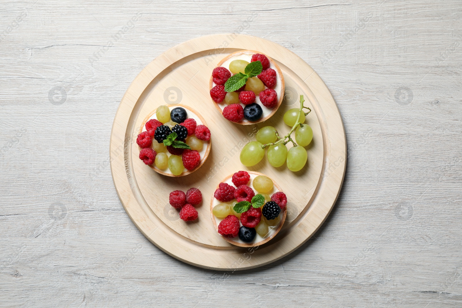 Photo of Delicious tartlets with berries on light wooden table, top view