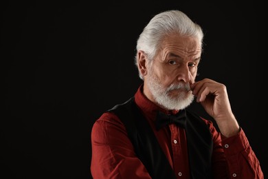 Photo of Senior man touching mustache on black background, space for text