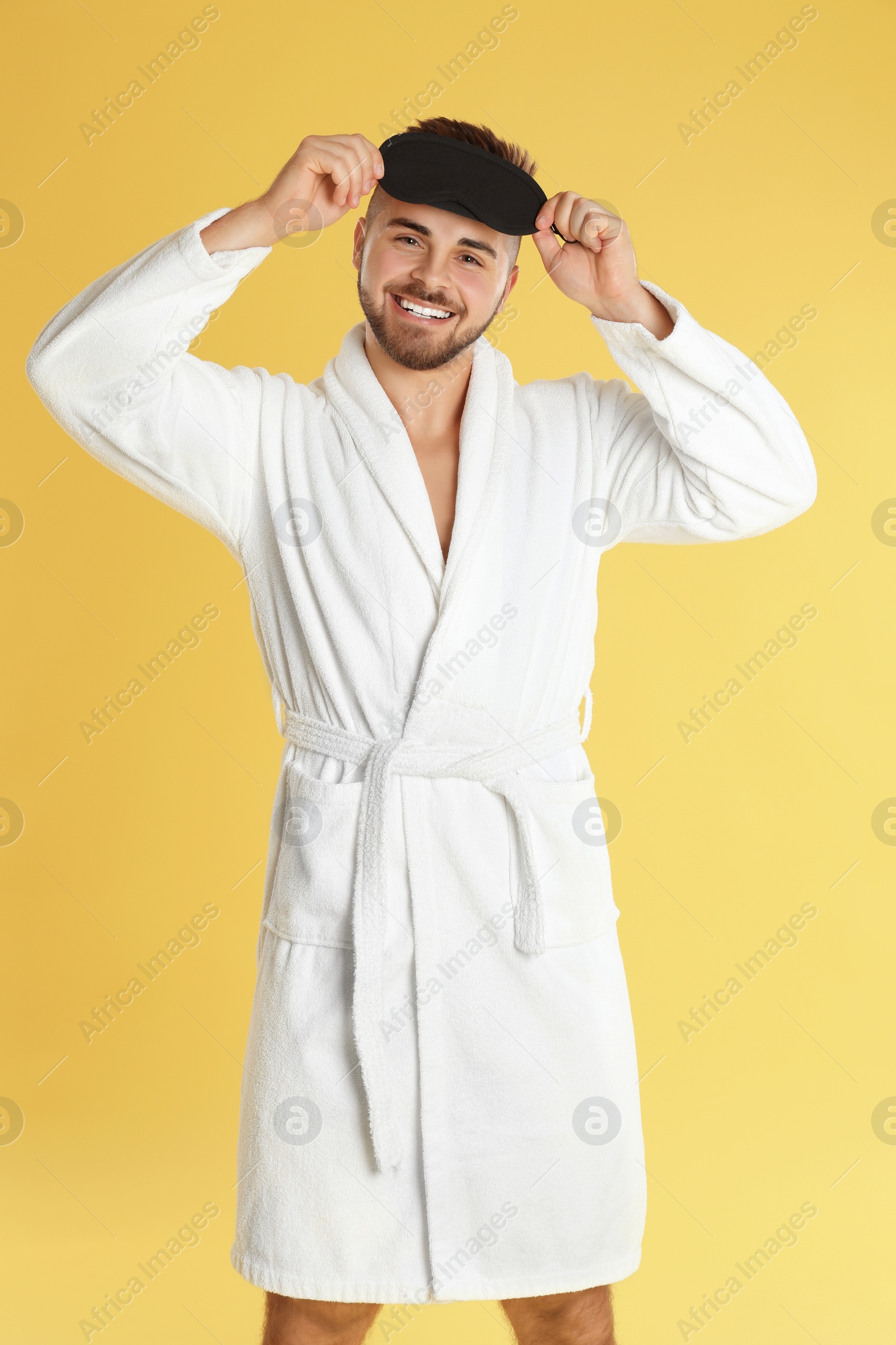 Photo of Young man in bathrobe and eye sleeping mask on yellow background