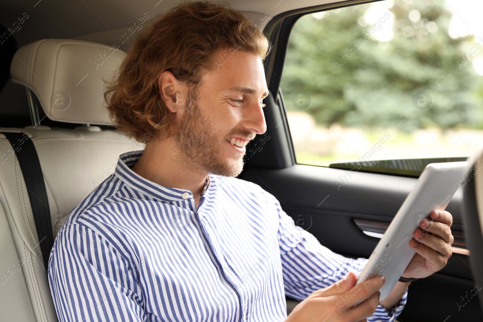 Photo of Attractive young man with tablet on backseat in luxury car