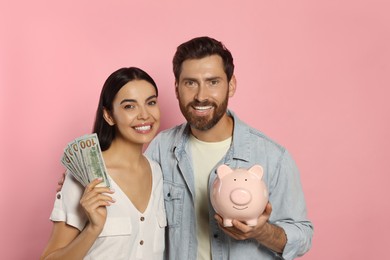 Happy couple with money and ceramic piggy bank on pale pink background