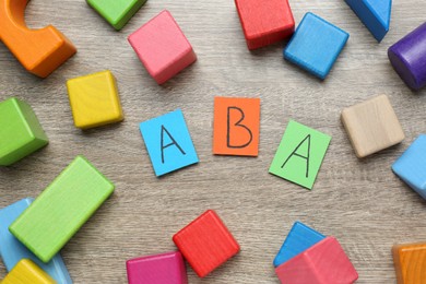 Photo of Colorful building blocks and cards with abbreviation ABA on wooden table, flat lay