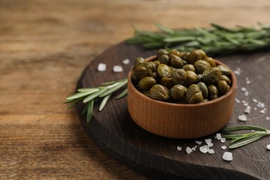 Photo of Bowl of capers, salt and rosemary on wooden table, space for text