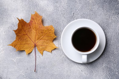 Cup of hot drink and autumn leaf on light grey textured table, flat lay