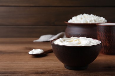 Photo of Clay bowl with sour cream on wooden table, space for text