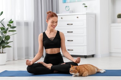 Beautiful woman with cute red cat practicing yoga on mat at home