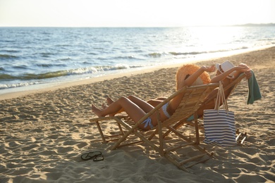 Photo of Young couple relaxing in deck chairs on beach near sea