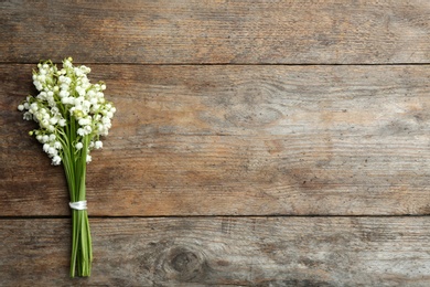 Beautiful lily of the valley bouquet on wooden background, top view. Space for text