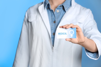 Doctor holding medical business card on color background, closeup. Women's health service