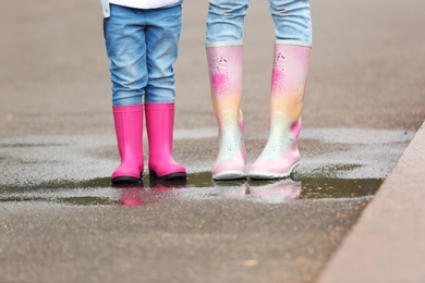 Photo of Mother and daughter wearing rubber boots on street, closeup