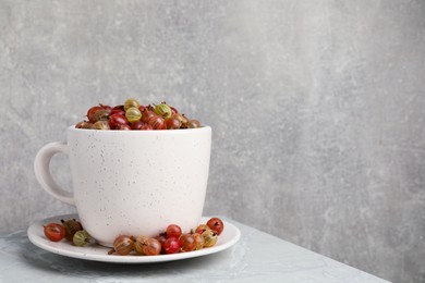 Cup with ripe gooseberries on light grey marble table, space for text