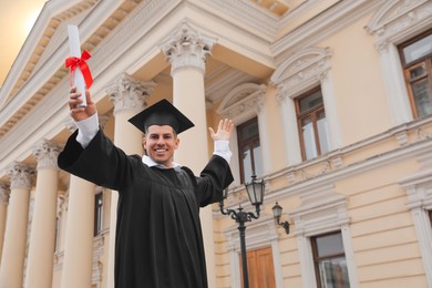 Photo of Happy student with diploma after graduation ceremony outdoors, low angle view. Space for text