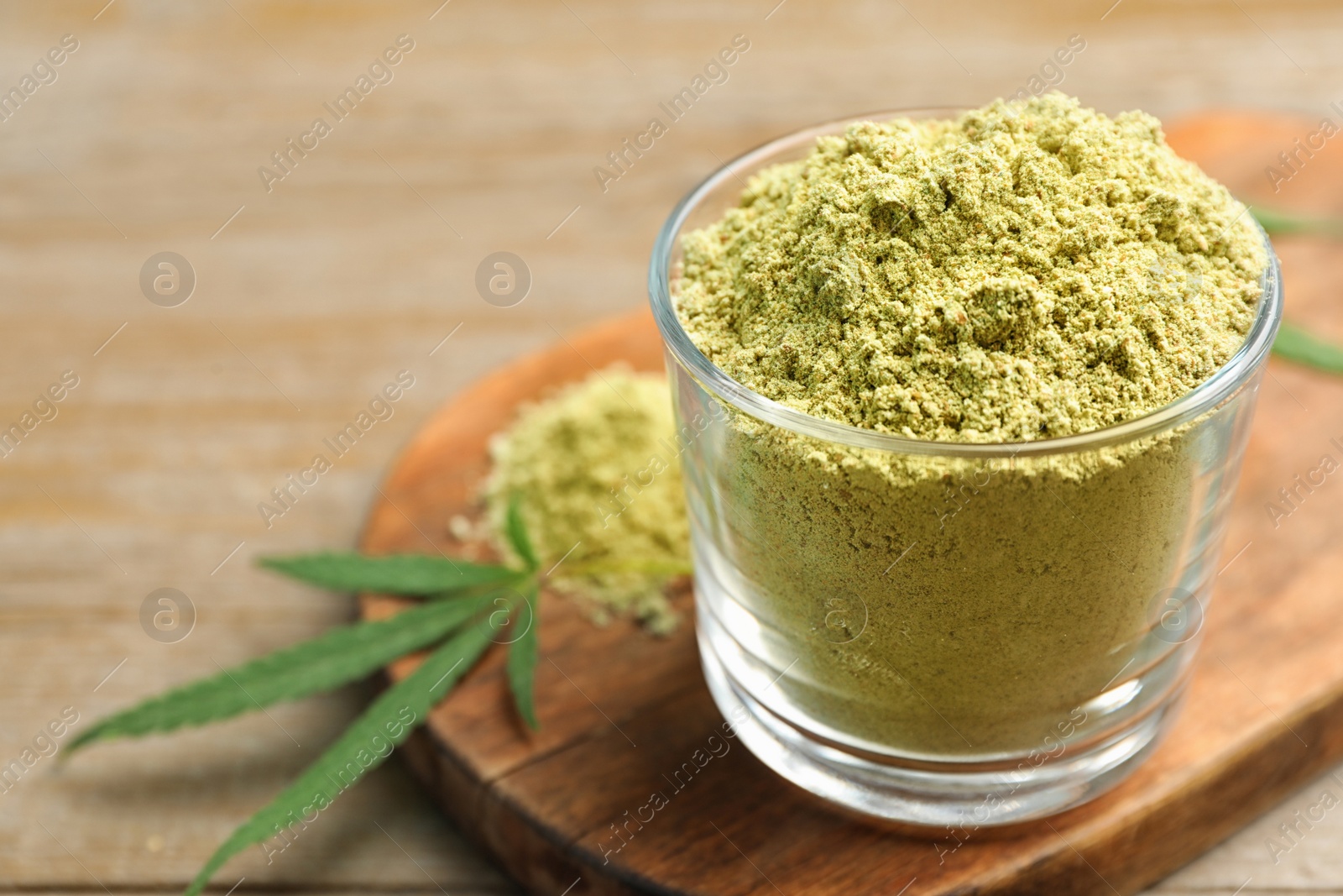 Photo of Glass of hemp protein powder on wooden table, closeup. Space for text