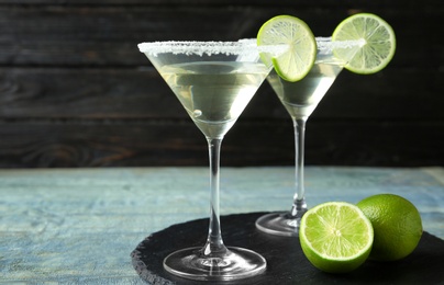 Photo of Glasses of Lime Drop Martini cocktail on light blue wooden table against dark background. Space for text