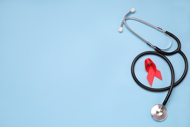 Photo of Red ribbon and stethoscope on light blue background, flat lay with space for text. AIDS disease awareness