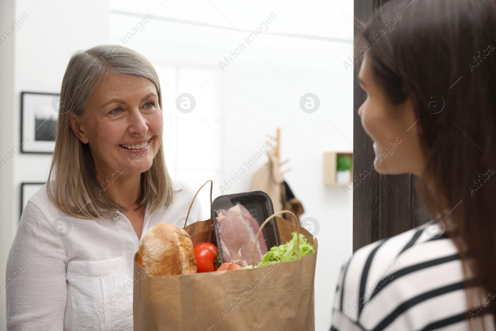 Photo of Courier giving paper bag with food products to senior woman indoors