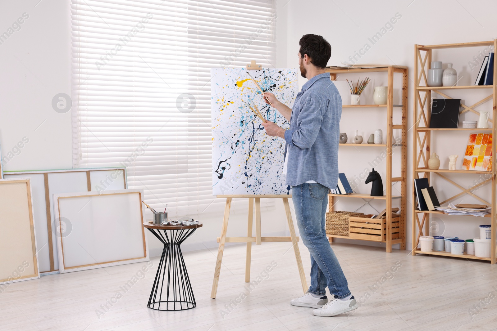 Photo of Man painting in studio, back view. Using easel to hold canvas