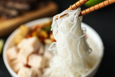 Photo of Chopsticks with tasty cooked rice noodles over bowl, closeup. Space for text