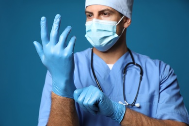 Photo of Doctor in protective mask putting on medical gloves against blue background