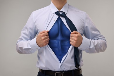 Businessman wearing superhero costume under suit on light grey background, closeup