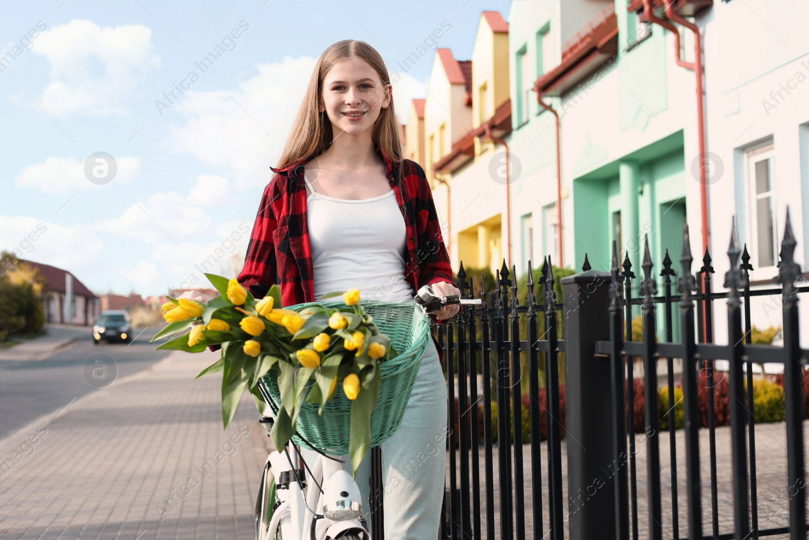 Photo of Beautiful teenage girl with bicycle and bouquet of yellow tulips on city street