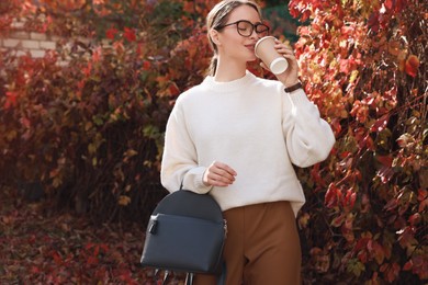 Photo of Beautiful young woman with stylish grey backpack drinking coffee in autumn park