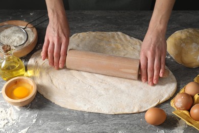 Photo of Woman rolling raw dough at grey table, closeup