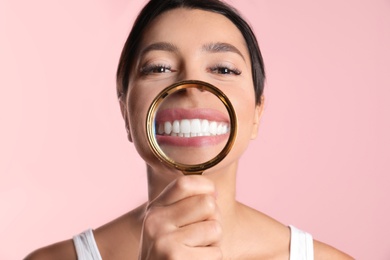 Young woman with healthy teeth and magnifier on color background