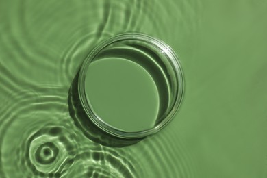 Photo of Stylish presentation for product. Glass podium in water on pale green background, top view