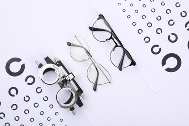 Vision test charts, glasses and trial frame on white background, flat lay