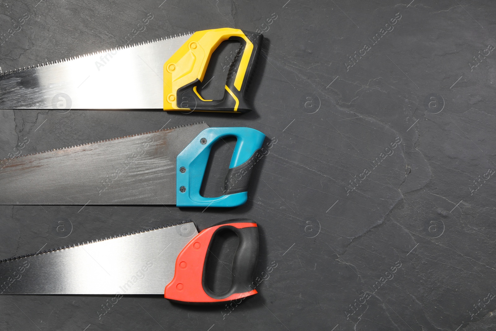Photo of Saws with colorful handles on black textured background, flat lay. Space for text