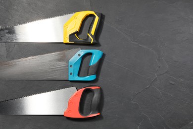 Saws with colorful handles on black textured background, flat lay. Space for text