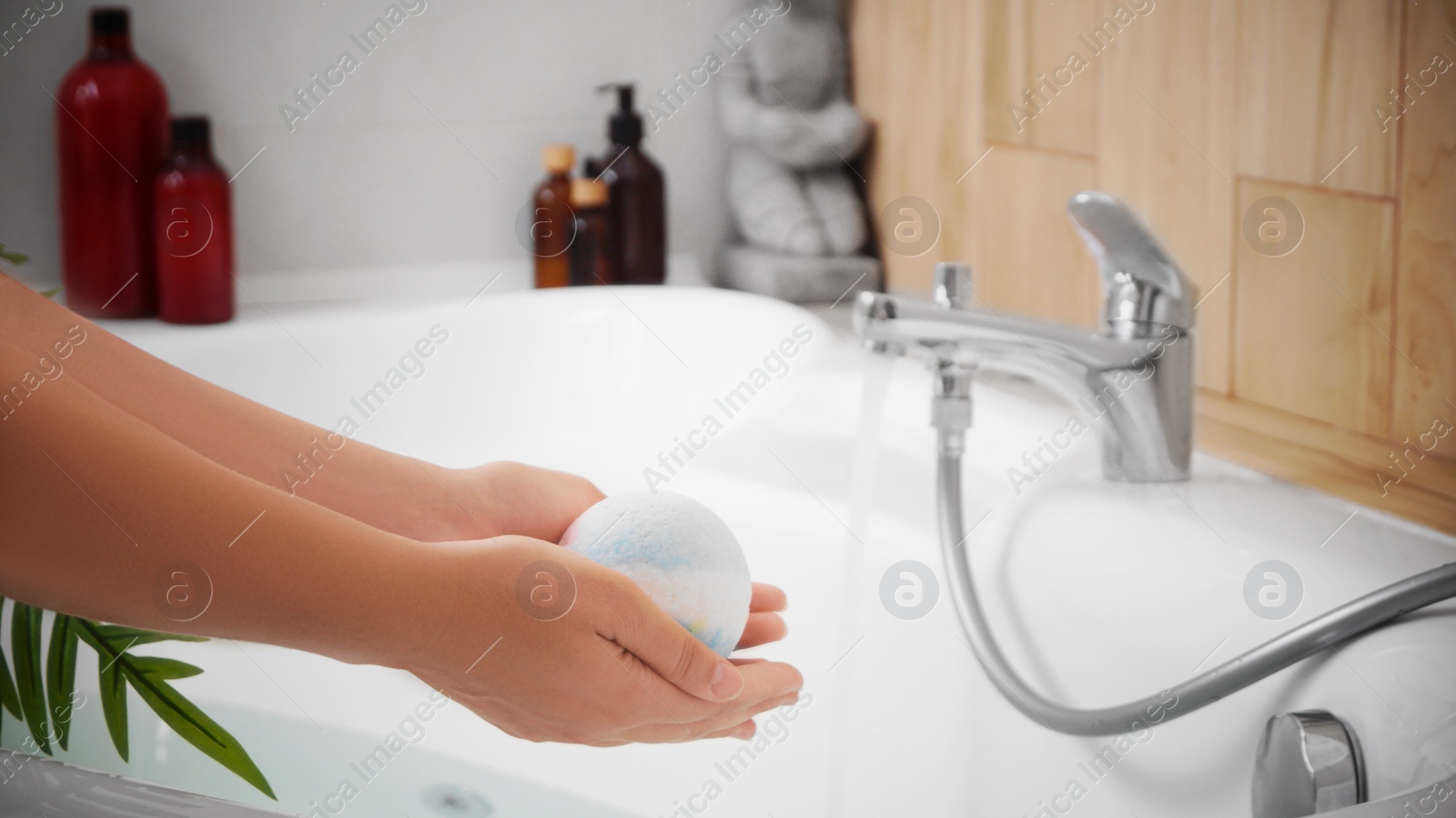 Photo of Woman holding bath bomb above tub indoors, closeup. Space for text