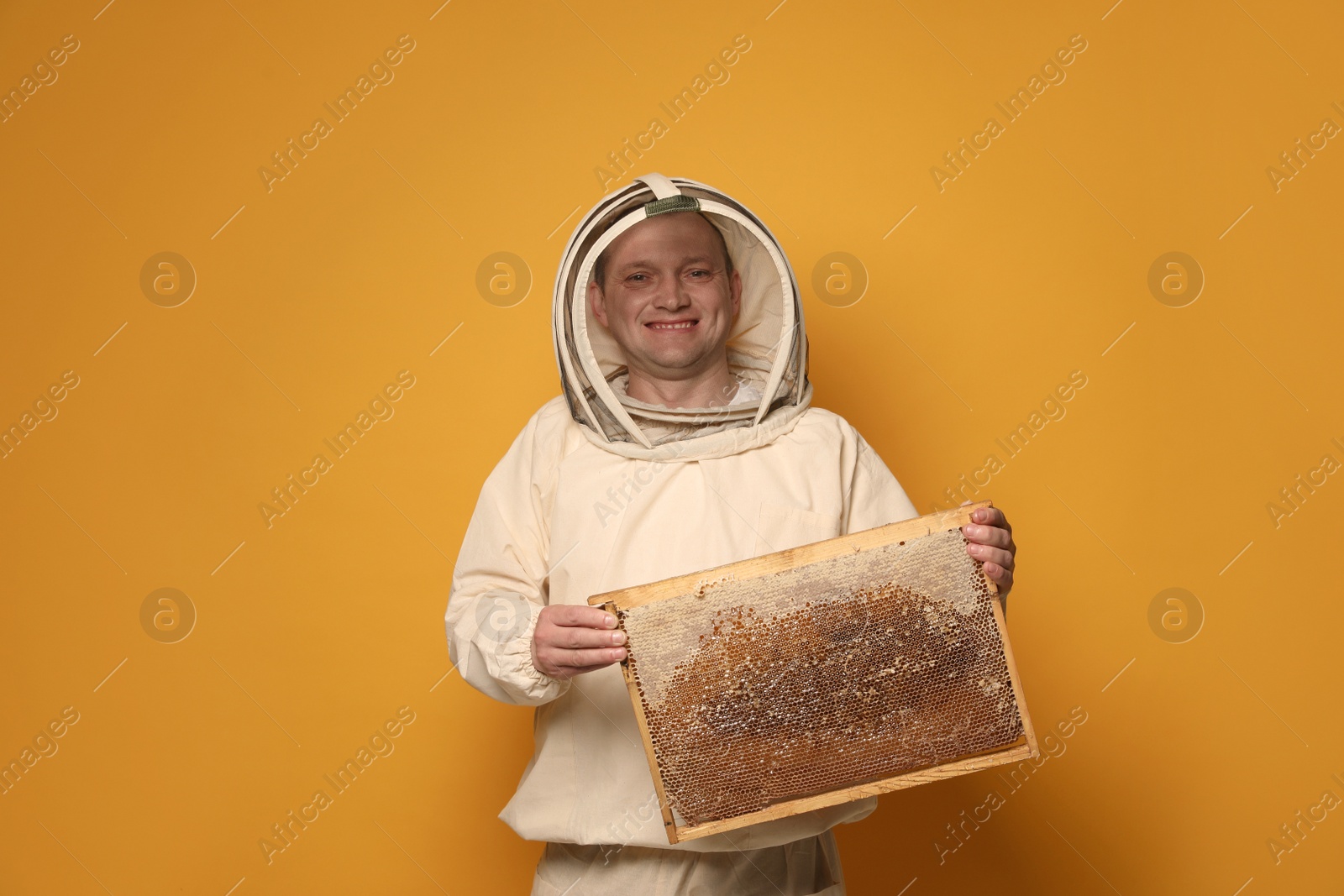 Photo of Beekeeper in uniform holding hive frame with honeycomb on yellow background