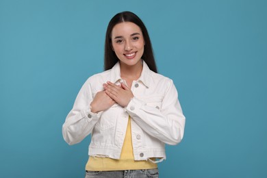 Photo of Thank you gesture. Beautiful grateful woman with hands on chest against light blue background