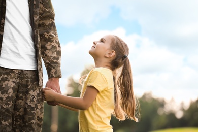 Photo of Little girl with her father in military uniform at sunny park