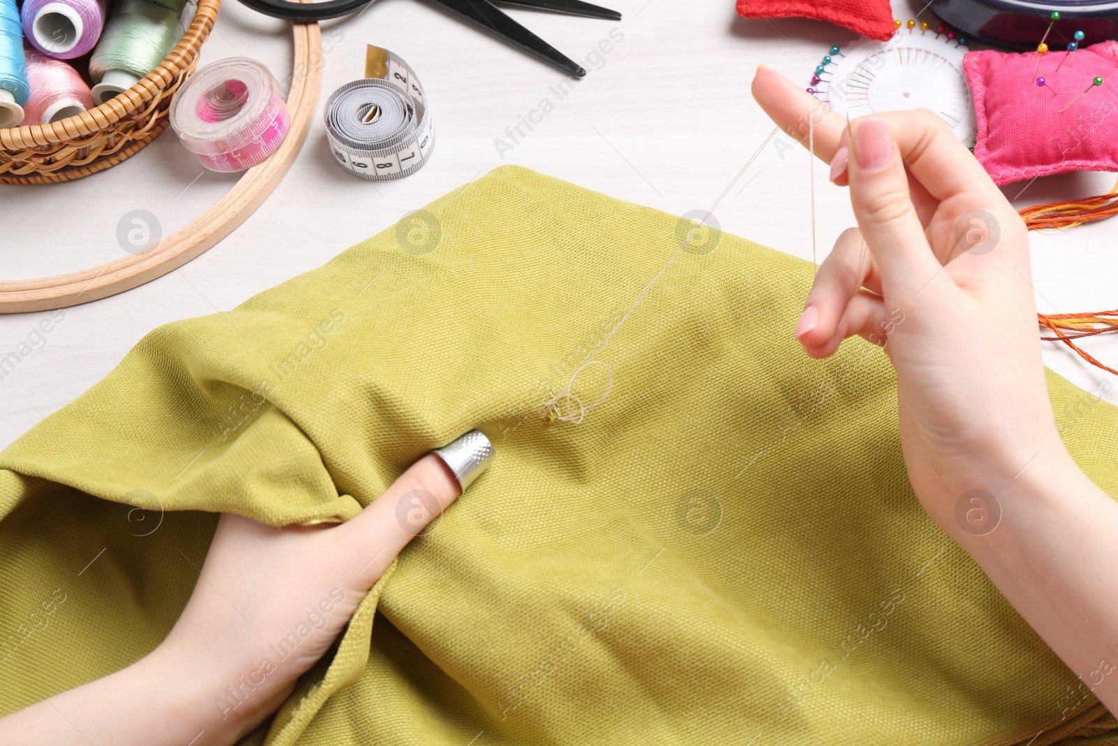 Photo of Woman with sewing thread embroidering on cloth at white table, closeup