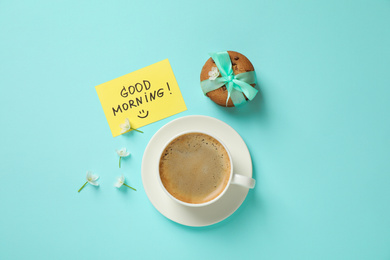 Photo of Delicious coffee, cookies, flowers and card with GOOD MORNING wish on light blue background, flat lay
