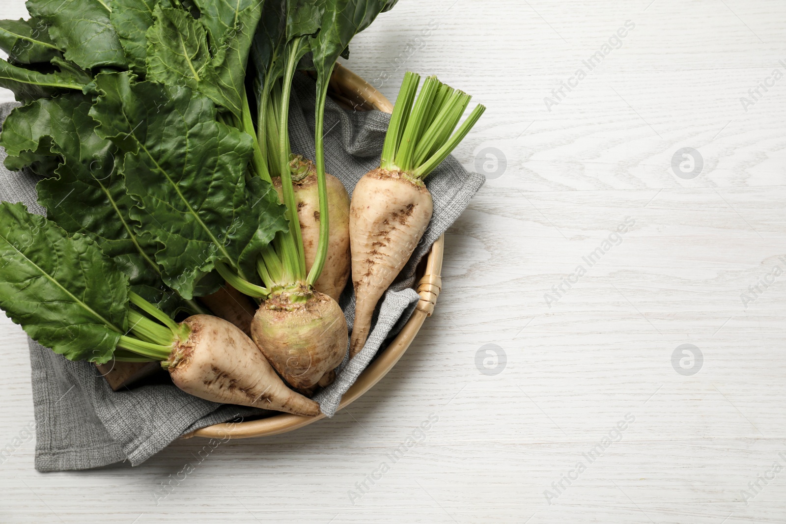 Photo of Basket with fresh sugar beets on white wooden table, top view. Space for text