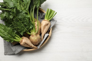 Photo of Basket with fresh sugar beets on white wooden table, top view. Space for text